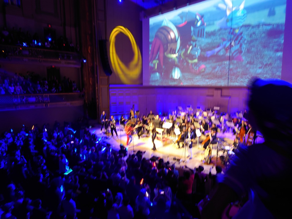 Another picture of the performers except it's kinda blurry because my hand slipped. Some stuff from Sonic and the Black Knight is up on the screen.